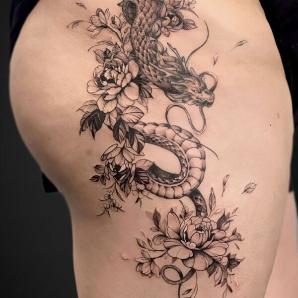 Black-and-gray tattoo of a curling snake weaving through peony flowers on the upper arm.