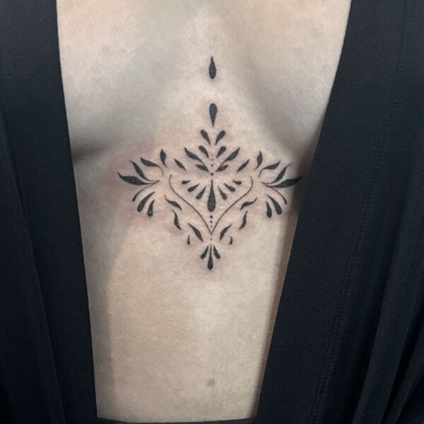 Symmetrical ornamental chest tattoo with leaf-like flourishes centered on the sternum.
