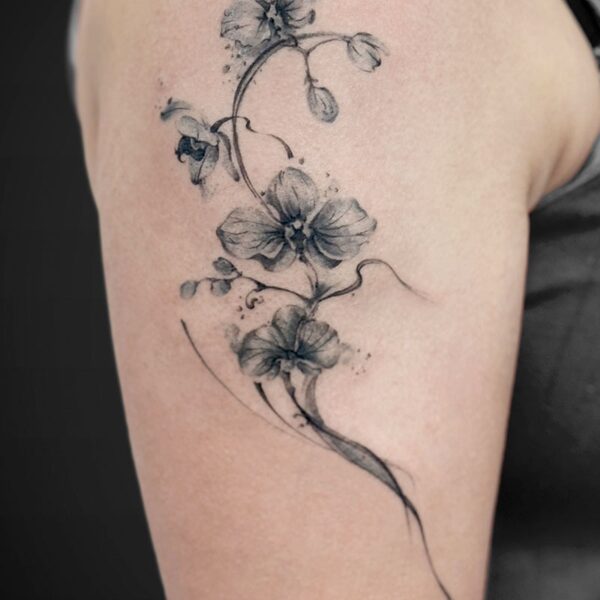 Black-and-gray floral tattoo along the upper arm, showing a cascading vine with several delicate flowers.
