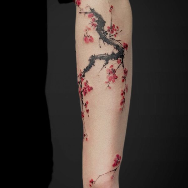 Forearm tattoo of a dark, gnarled branch winding around with pink cherry blossoms scattered along the limb.