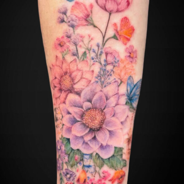 colour-realism-tattoo-flowers-butterflies Colorful floral tattoo on the forearm with a large purple daisy-like bloom, pink and orange flowers, green leaves, and two blue butterflies.
