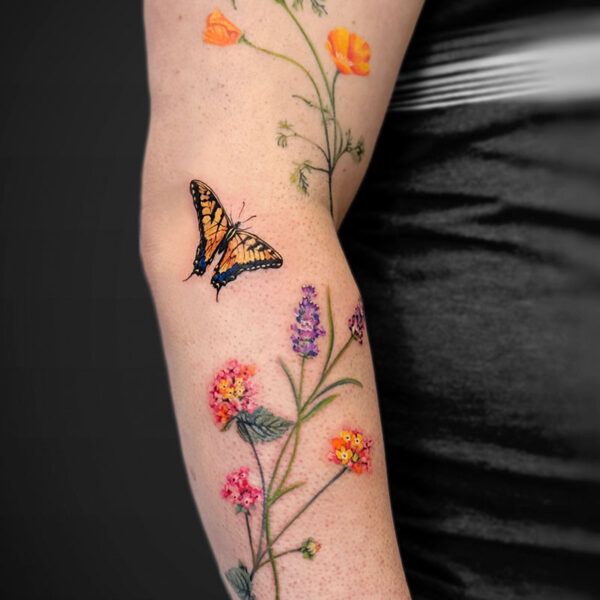 Forearm tattoo of tall wildflowers with orange poppies, purple and pink blossoms, and a yellow-and-black butterfly.