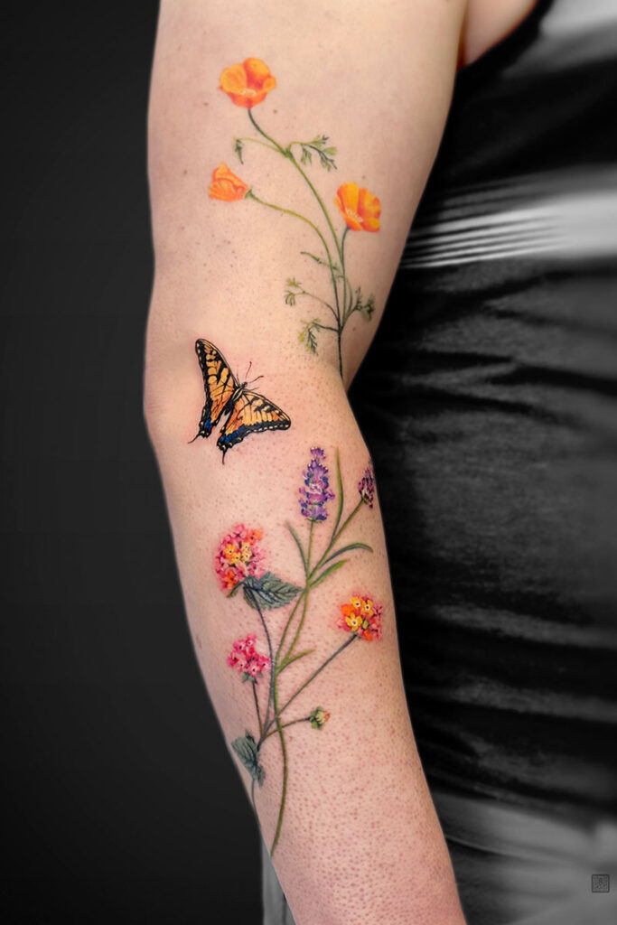 Forearm tattoo of tall wildflowers with orange poppies, purple and pink blossoms, and a yellow-and-black butterfly.