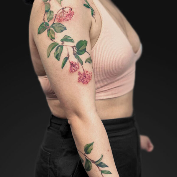 Side view of a person with a pink floral tattoo sleeve running from shoulder to forearm, wearing a light pink sports bra and black pants.