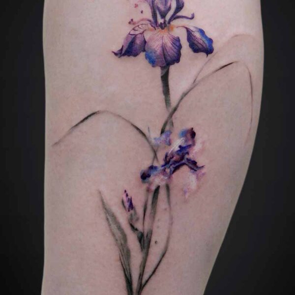 Watercolor-style purple iris tattoo along the back of a leg with delicate green stems and leaves.