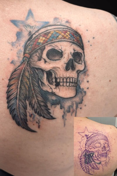 Color tattoo of a skull wearing a patterned headband, with a long feather and blue watercolor splash behind it.