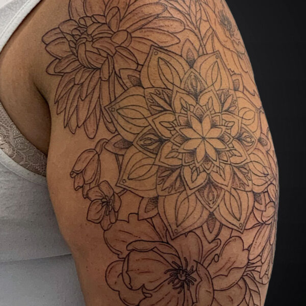 Line-drawing tattoo sleeve on upper arm with a central mandala and surrounding large flowers and leaves in intricate, outline-only style.
