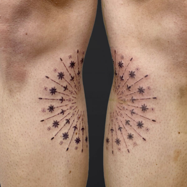 Two knees viewed from behind, each with a matching radial starburst tattoo around the back of the knee.