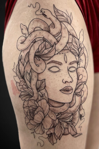 Tattoo design of a woman's face surrounded by curling snakes and leafy flowers.