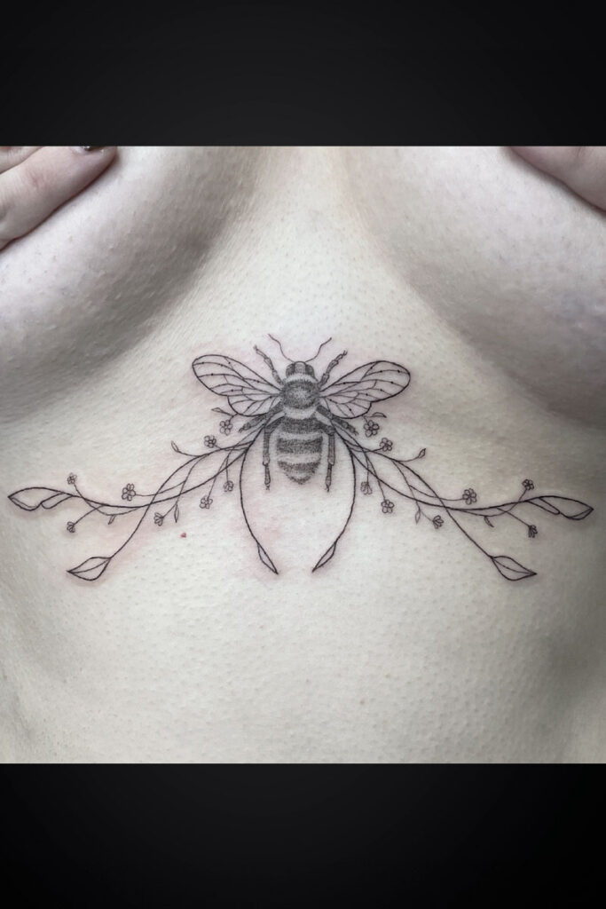 Delicate line tattoo of a bee centered on the back of the neck, with a floral vine extending left and right and small blossoms along the stems.