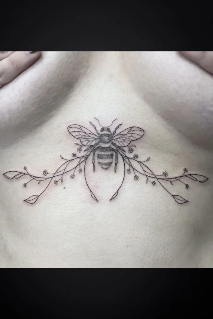 Delicate line tattoo of a bee centered on the back of the neck, with a floral vine extending left and right and small blossoms along the stems.