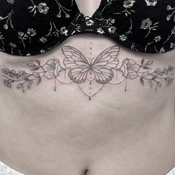 Delicate butterfly tattoo across the lower chest with floral vines and dangling dotted jewelry lines.