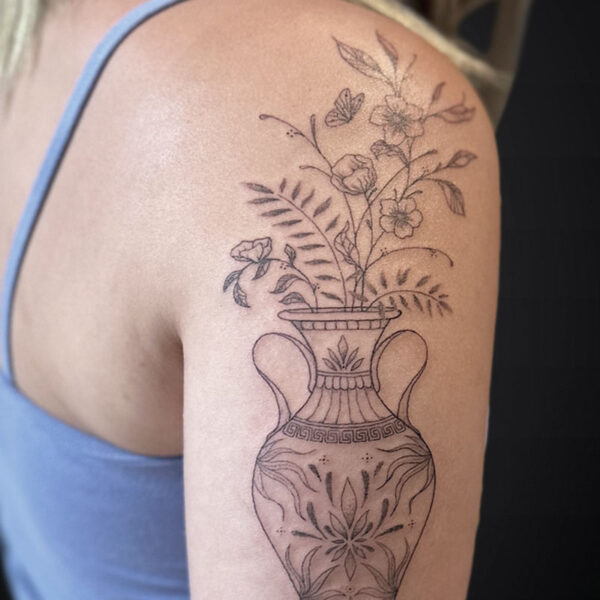 Line drawing tattoo of an ornate vase with blooming flowers on a person's upper arm.