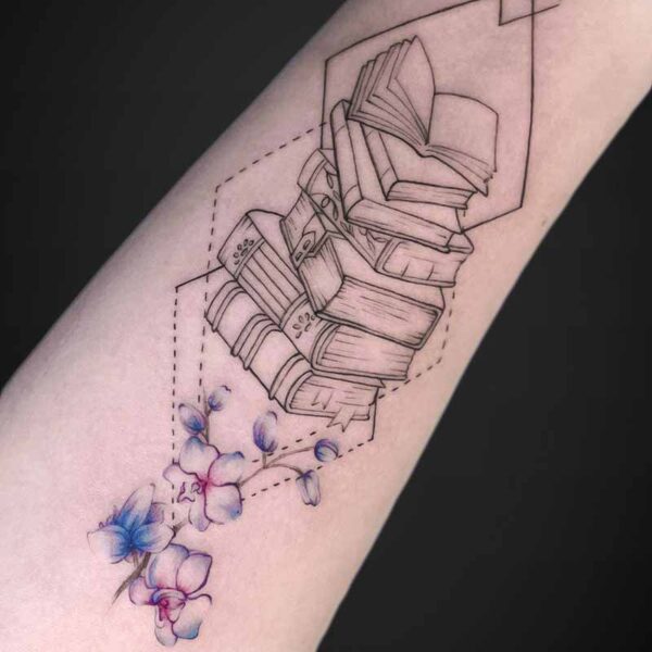 Forearm tattoo showing a stack of books inside a geometric outline, with blue‑violet flowers at the base.
