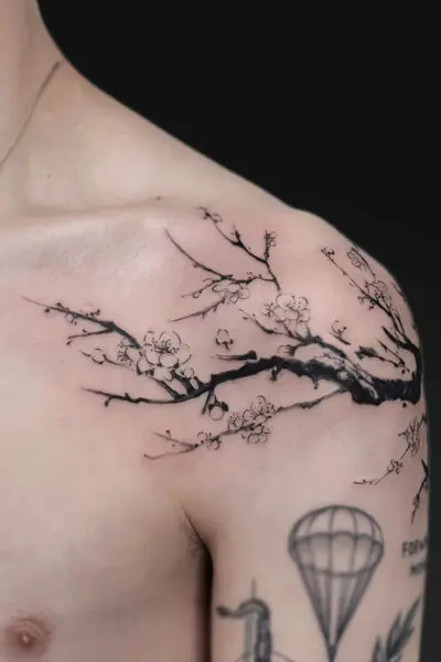 Black ink cherry blossom branch wraps across the shoulder and chest, with delicate blossoms; a hot air balloon tattoo peeks at the lower arm.