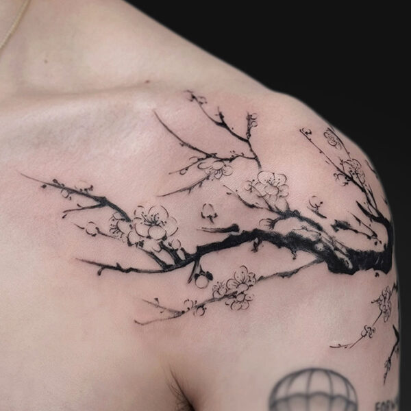 Black ink cherry blossom branch wraps across the shoulder and chest, with delicate blossoms; a hot air balloon tattoo peeks at the lower arm.