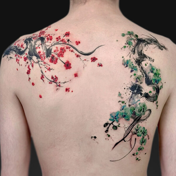 Back view of a person with a watercolor-style tattoo across the shoulders: red cherry blossoms and branches on the left, green-blue foliage and black ink strokes on the right.