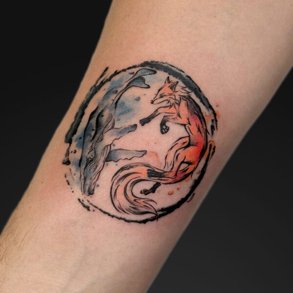 Tattoo on forearm: a red fox leaping inside a circular black brushstroke frame with blue wave-like accents.