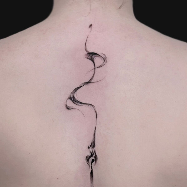Back view of a person with a slender, spiraling black tattoo running down the spine, ending in a small pendant-like tip.