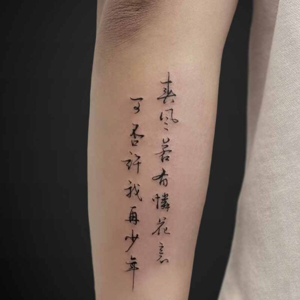 Close-up of a forearm showing a vertical line of black ink calligraphy tattoo running along the inner arm.