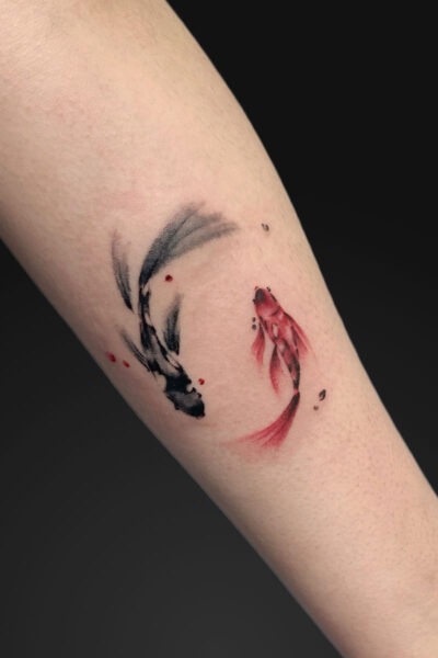 Watercolor-style koi fish tattoo in black and red on a forearm, depicted in a curved, flowing loop with splashes of red.