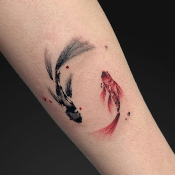 Watercolor-style koi fish tattoo in black and red on a forearm, depicted in a curved, flowing loop with splashes of red.