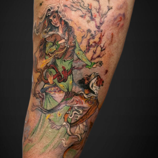Colorful fantasy tattoo on forearm showing a green-clad woman with flowing hair and a figure amid twisting tree branches and leaves.