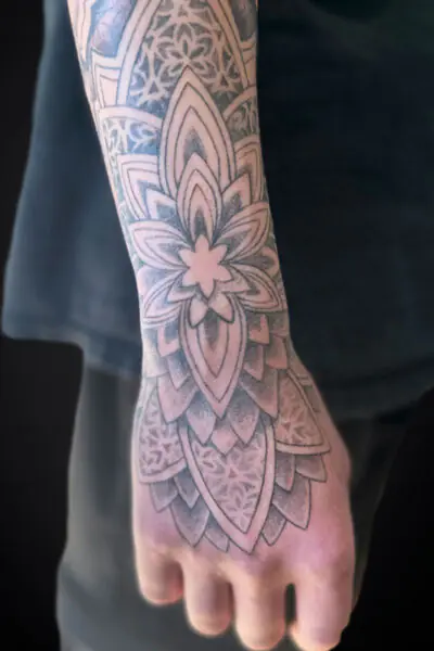 Close-up of a forearm tattoo with a detailed black-and-gray mandala pattern extending toward the wrist and hand.