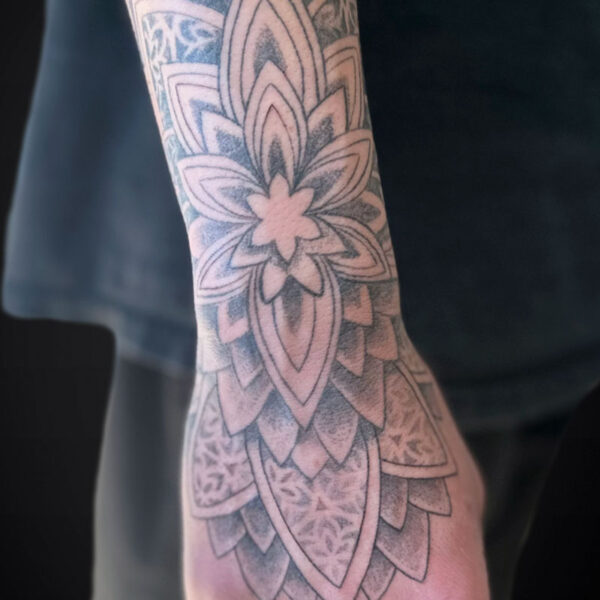 Close-up of a forearm tattoo with a detailed black-and-gray mandala pattern extending toward the wrist and hand.