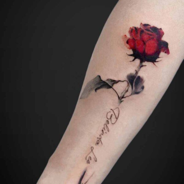 Forearm tattoo of a red rose with black shading and a cursive word along the arm described.