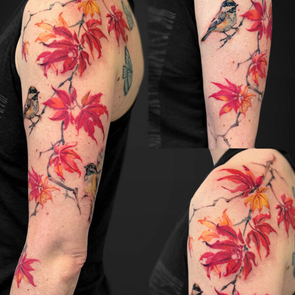 Colorful tattoo sleeve on the upper arm with red‑orange maple leaves and small birds perched on branches.