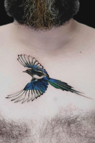 Blue and green swallow tattoo in mid-flight across the upper chest, wings spread wide near the collarbone.