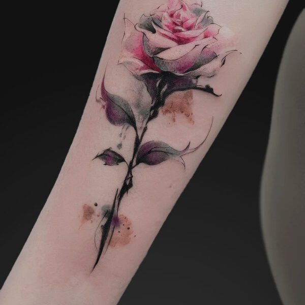 Watercolor pink rose tattoo on forearm with a black stem and subtle color washes.