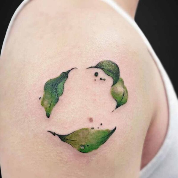 Watercolor-style tattoo on the upper arm forming a simple smiling face with green leaves.