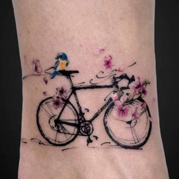 Delicate bicycle tattoo with pink blossoms and a blue bird perched on the handlebars.